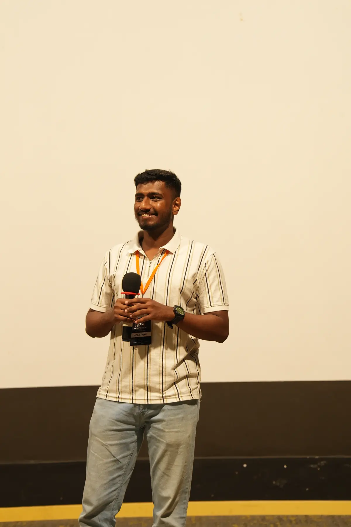 Nithin Daniel speaking on stage with a microphone at a tech event in India